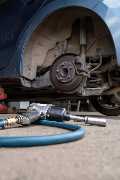 Outil de clé pneumatique sur l'asphalte et un cric de voiture pour soulever le corps et changer le pneu. Voiture sans roue - Photo, image