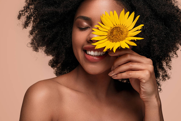 Happy African American woman touching face with flower - 写真・画像