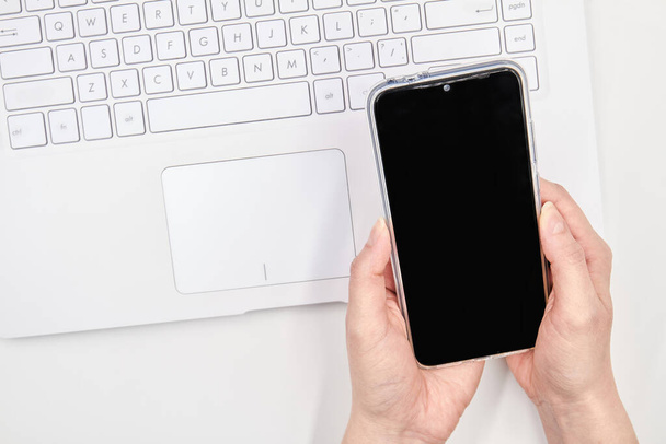 Mockup smartphone leeg scherm in vrouwelijke handen op de achtergrond van een witte laptop. Sluitingsdatum. - Foto, afbeelding