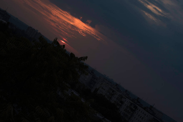 Um céu carmesim em um pôr do sol contrastante sobre uma grande cidade na Ucrânia, a cidade de Kharkiv nos últimos segundos e o sol desaparecerá atrás do horizonte, uma vista deslumbrante do dia que passa e o encontro da noite com o dia. Nuvens no horizonte em - Foto, Imagem