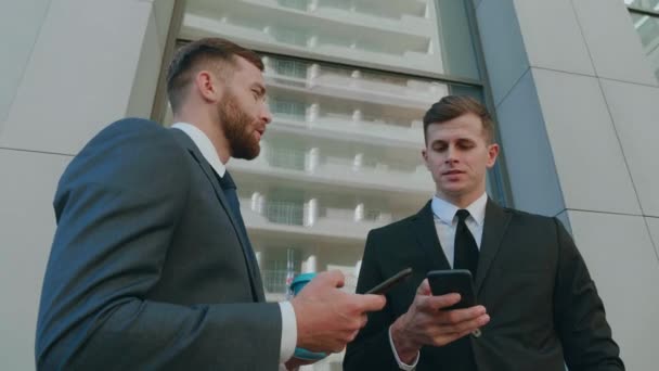 Два работника-мужчины взаимодействуют друг с другом в деловом районе города. Уверенные бизнесмены, использующие смартфон, обсуждают планирование бизнес-проекта в корпоративной командной работе - Кадры, видео