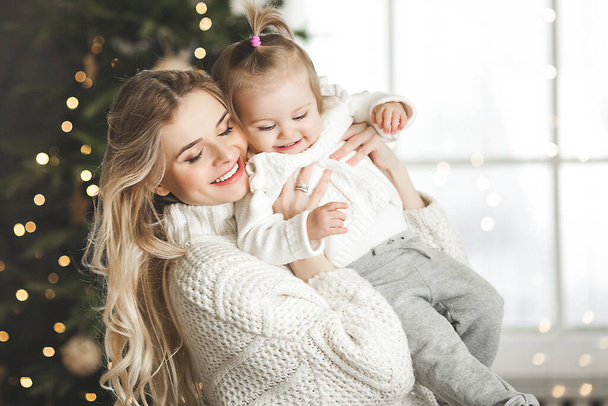 Приваблива молода мати зі своєю маленькою донькою на різдвяному фоні
 - Фото, зображення