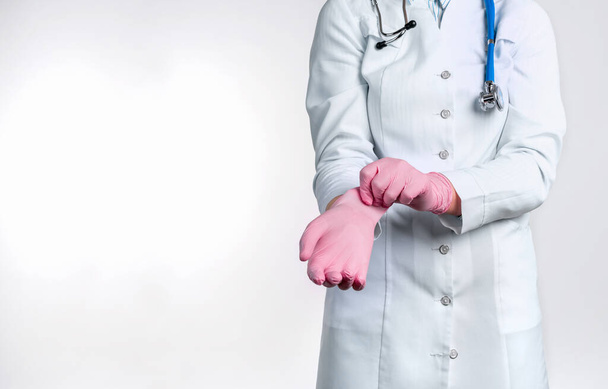 Widok kobiety w mundurze, zakładającej różowe, sterylne rękawiczki na białym tle. Koncepcja medyczna - Zdjęcie, obraz