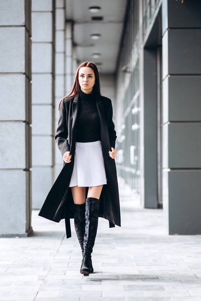 Portrait of a full-length girl on the street in autumn. Young adult girl in an elegant coat outdoors. Promotional coat. Young fashionable brunette woman in a stylish woolen autumn and spring coat. - Φωτογραφία, εικόνα