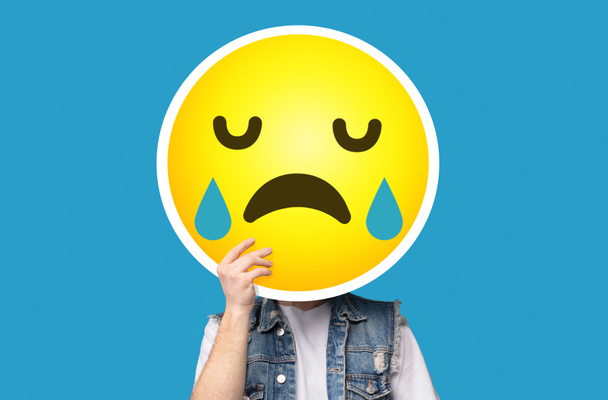 Unrecognizable man hiding his face behind crying sad emoticon emoji - Photo, Image