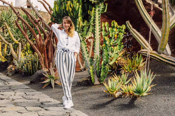 Atractiva joven posando con plantas en el jardín de cactus en la isla de Lanzarote, Islas Canarias - Foto, Imagen