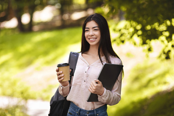Smiling Asian Student Girl With Backpack And Laptop Enjoying Takeaway Coffee Outdoors - Foto, imagen
