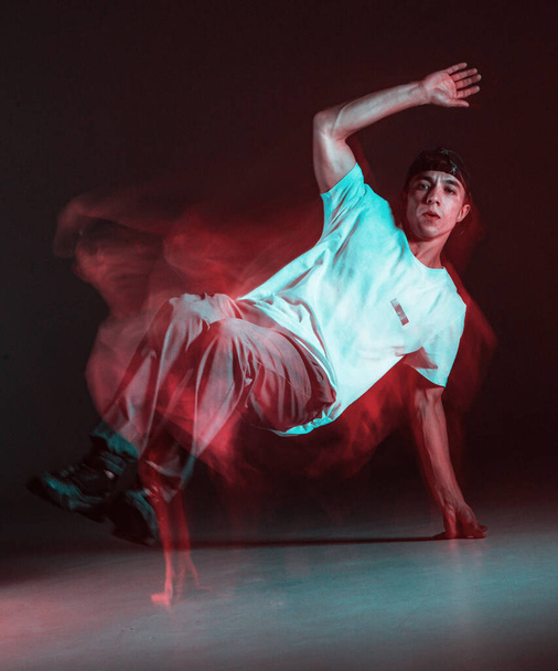 Stylish young guy breakdancer dancing hip-hop in neon light. Long exposure shot - 写真・画像