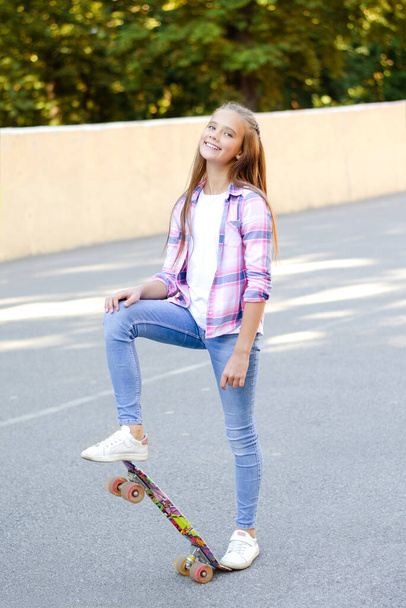 Smiling cute little girl child standing with a skateboard. Preteen with penny board outdoors in summer day - Foto, afbeelding