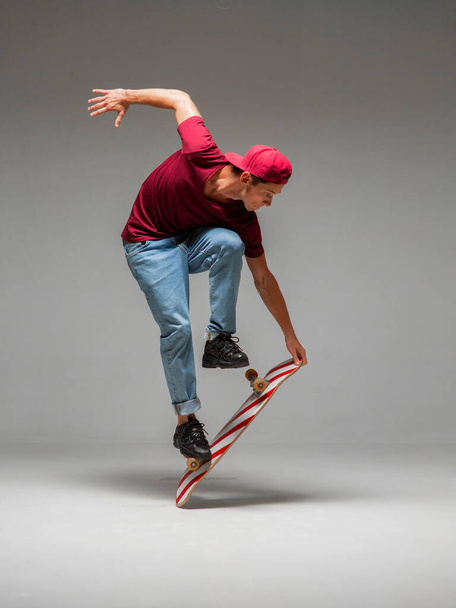 Stylish young guy skateboarder stands on skateboard in studio isolated on gray background. Skateboarding tricks - Foto, afbeelding