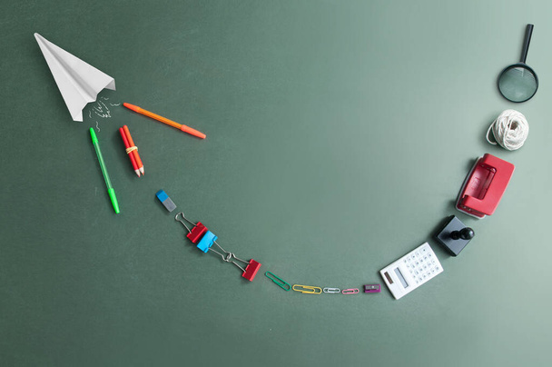 Trail of stationery behind a paper airplane on a green chalkboard - Fotografie, Obrázek