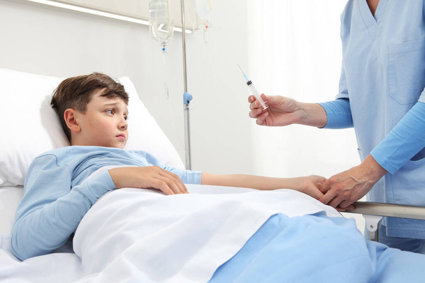 Ängstliches Kind liegt im Krankenhauszimmer in Angst vor der Spritzennadel und Krankenschwester gibt ihm eine Spritze - Foto, Bild
