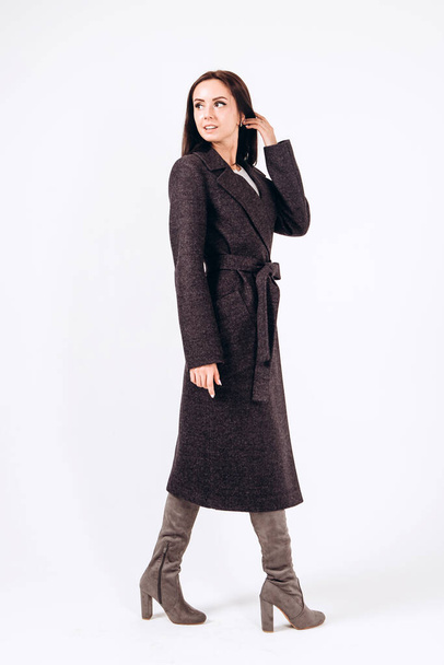 girl in a warm light coat on a white background. model in outerwear. brunette in a long black coat. beautiful girl in a casual coat. spring autumn collection. Portrait of a brunette coat, full growth. - Zdjęcie, obraz