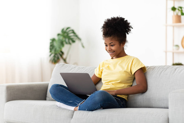 Africaine adolescent fille à l'aide d'ordinateur portable navigation sur Internet assis à la maison - Photo, image