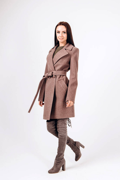 girl in a warm light coat on a white background. model in outerwear. brunette in a long beige coat. beautiful girl in a casual coat. spring autumn collection. Portrait of a brunette coat, full growth. - Φωτογραφία, εικόνα