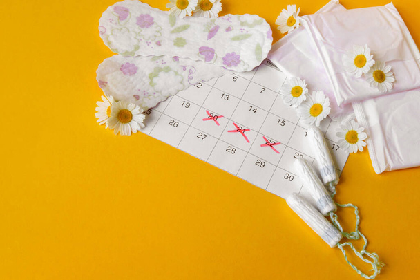 Menstrual pads and tampons on menstruation period calendar with chamomiles on yellow background. The concept of female health, personal hygiene during critical days. - Photo, Image