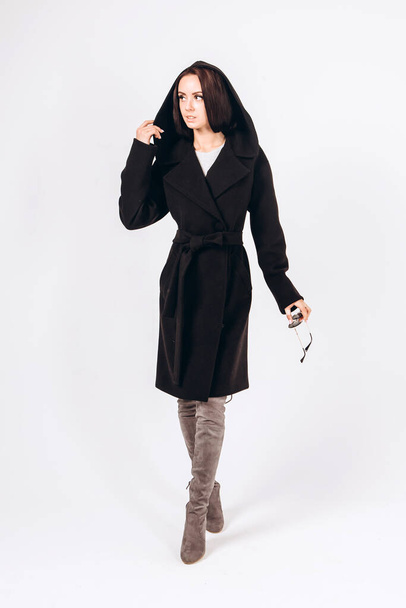 girl in a warm light coat on a white background. model in outerwear. brunette in a long black coat. beautiful girl in a casual coat. spring autumn collection. Portrait of a brunette coat, full growth. - 写真・画像