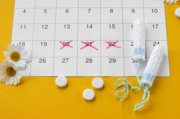 Menstruační tampóny na menstruačním kalendáři s heřmánky na žlutém pozadí. Koncept zdraví žen, osobní hygieny v kritických dnech. - Fotografie, Obrázek