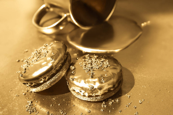 O ouro líquido flui de um copo dourado. Biscoitos dourados em um fundo dourado. - Foto, Imagem