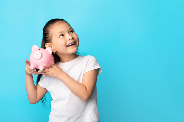 Little girl with piggy bank, studio shot, free space - Photo, Image