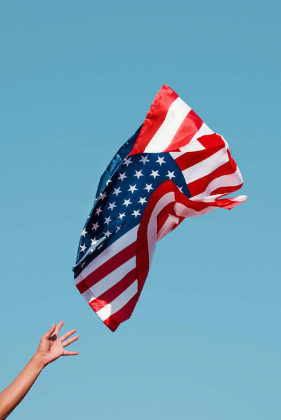 közelkép egy fiatal kaukázusi férfiról, aki fellövi az Egyesült Államok zászlaját a kék ég felé, vagy éppen azon van, hogy elkapja, amint a levegőben repül. - Fotó, kép
