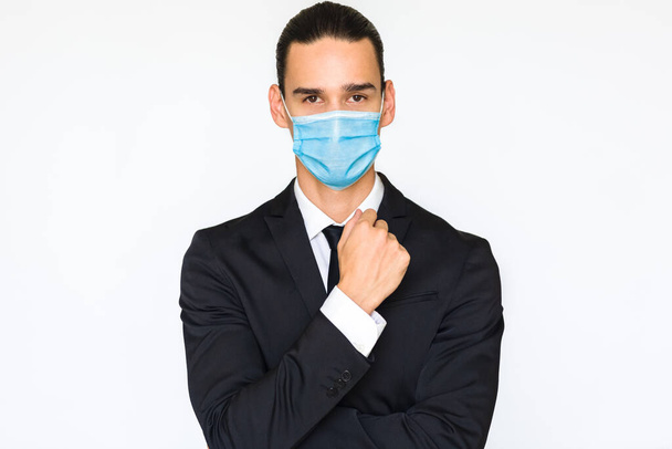Πορτρέτο ενός κλασάτου νεαρού επιχειρηματία που φοράει ιατρική μάσκα προσώπου. Απομονωμένο σε λευκό φόντο και κοιτάζοντας την κάμερα. - Φωτογραφία, εικόνα