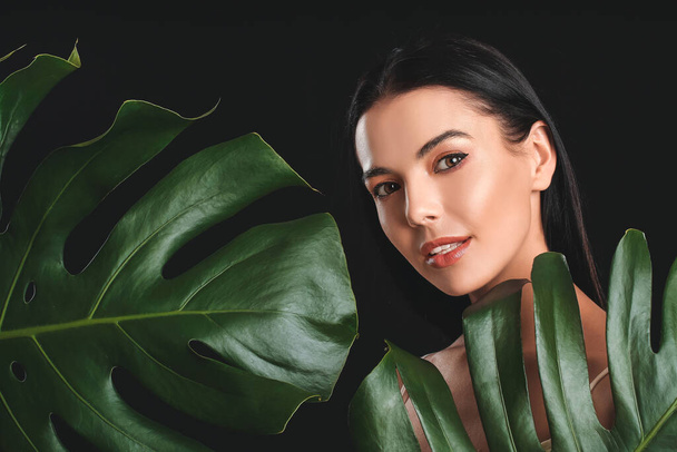 Young woman with beautiful eyeshadows and tropical leaves on dark background - Fotoğraf, Görsel