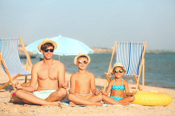 Man and his children meditating on sea beach at resort - Fotoğraf, Görsel