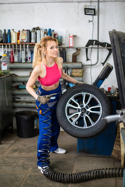 una chica en un servicio de coches trabaja con neumáticos - Foto, imagen