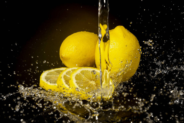 Lemon with drops and splashes of water on a black background - Foto, Bild