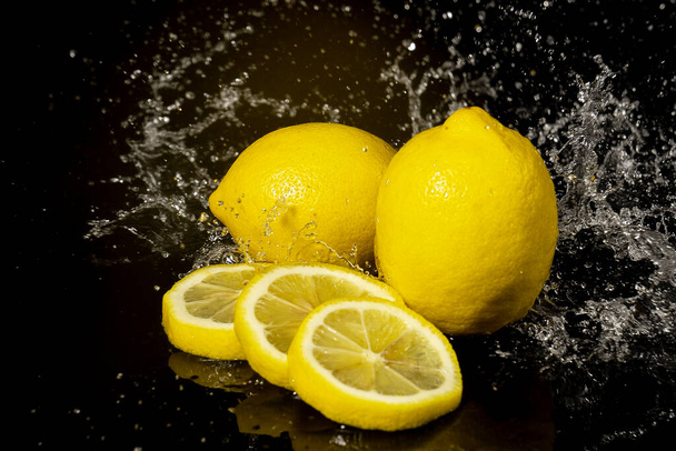 黒の背景に水の滴とスプラッシュレモン - 写真・画像