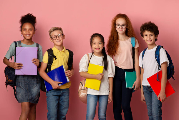Multiethnic group of kids ready for school with backpacks and copybooks on pink background - Photo, Image