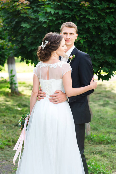 Молода пара щойно одружилася. Весільна пара ніжно обіймається в зеленому саду, наречена стоїть назад до пострілу
 - Фото, зображення