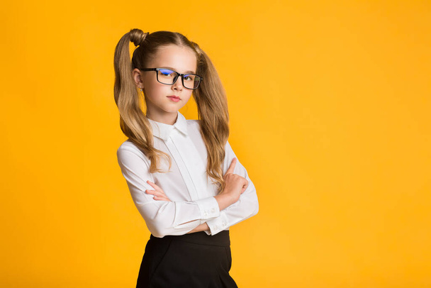 Serious Elementary School Girl Posing Crossing Hands Over Yellow Background - Foto, Imagem