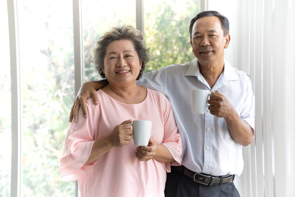 Szczęśliwa azjatycka para seniorów uśmiechnięta podczas picia porannej kawy w domu. Styl życia emerytalnego. - Zdjęcie, obraz