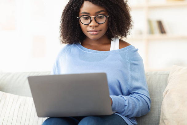 Focused black woman sitting on couch with pc - Foto, Bild