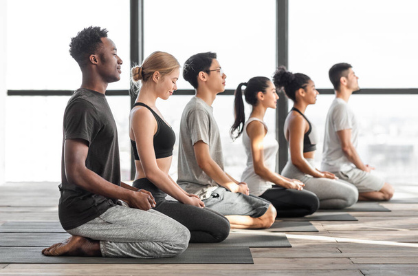 Happy multiracial men and woman practicing yoga and meditating together in studio - Photo, Image