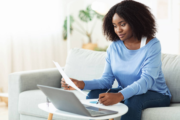 黒人女性は自宅でノートパソコンで働く書類に署名する - 写真・画像