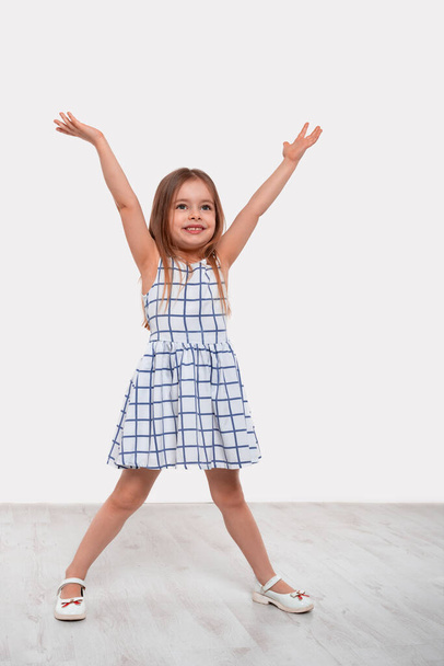 Full length portrait of  little happiness girl with long blonde hair raising her hands up rejoicing at something against white background in studio. - Foto, imagen