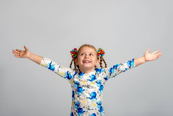 Una piccola ragazza felice con due code con nastri colorati alzò le mani esultando per qualcosa su uno sfondo bianco. - Foto, immagini