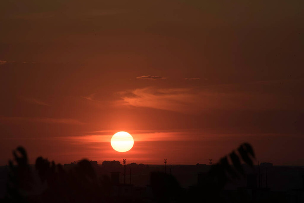 Um céu carmesim em um pôr do sol contrastante sobre uma grande cidade na Ucrânia, a cidade de Kharkiv nos últimos segundos e o sol desaparecerá atrás do horizonte, uma vista deslumbrante do dia que passa e o encontro da noite com o dia. Nuvens no horizonte em - Foto, Imagem
