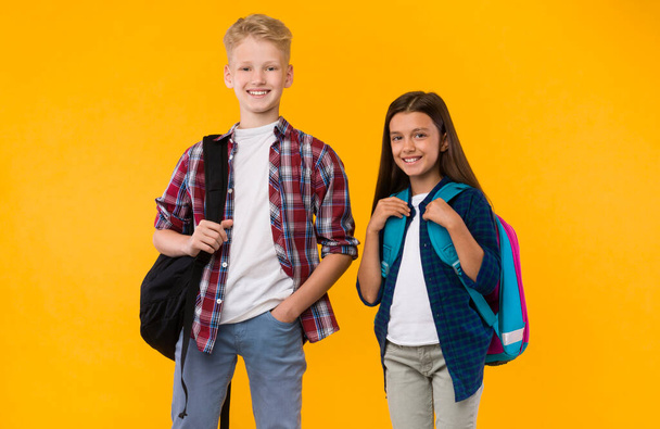 Casual schoolchildren standing with backpacks on yellow studio - Foto, Imagem