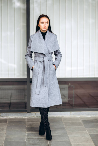 girl in a warm coat outdoors. model in outerwear. brunette in a long gray coat walks around the city. beautiful girl in a fashionable casual coat. spring autumn collection. - Valokuva, kuva