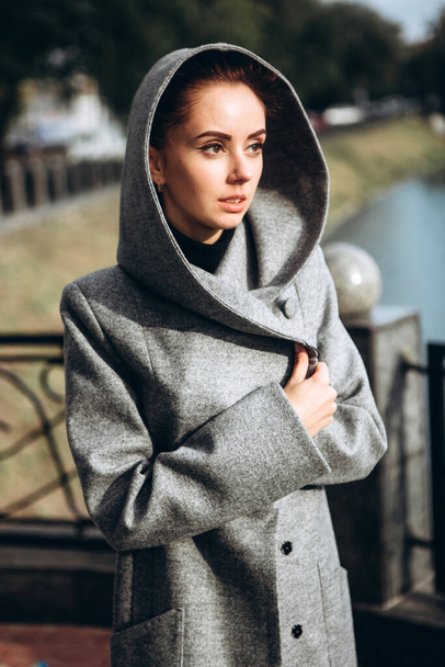 girl in a warm coat outdoors. model in outerwear. a brunette in a long gray coat walks along the embankment of the river. beautiful girl in a fashionable casual coat. spring autumn collection. - Fotografie, Obrázek