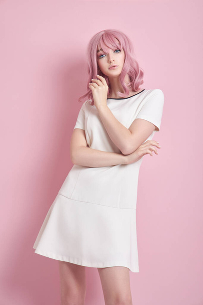 Beautiful girl with pink hair, hair coloring. Cute anime woman stands on a pink background in a short white dress. Colored hair, perfect hairstyle - Фото, изображение