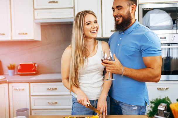 Cheerful smiling couple cooking and drinking wine in kitchen - Zdjęcie, obraz