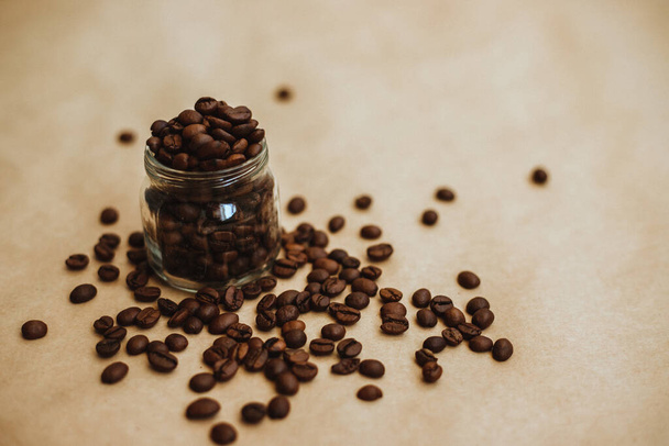 Coffee beans in a glass jar. Dark-colored roasted coffee beans on Kraft paper. Texture. - Foto, Imagem