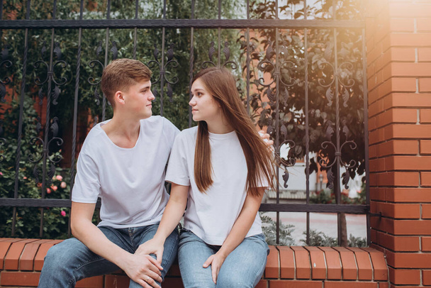 A young couple on a fall day walk around the city. A happy couple is sitting on a brick fence and laughing. Real emotions. Couple close up portrait. A man and a woman walk outdoors on a sunny day. - Photo, image