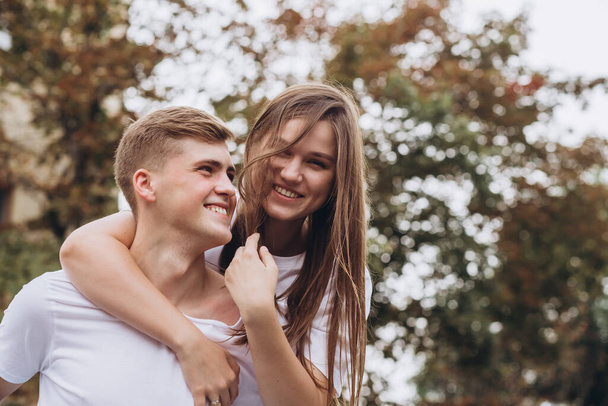 幸せな若いカップルは街の通りを歩いて手をつないでください。白いTシャツとジーンズを着た男と女が屋外で。秋の木を背景にした10代の若者たち。カップルクローズアップ肖像画 - 写真・画像