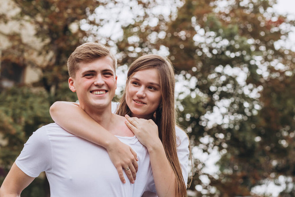 Happy young couple walks the streets of the city and hold hands. guy and girl in white t-shirts and jeans outdoors. Teenagers cuddling against the backdrop of an autumn tree. Couple close-up portrait - Fotografie, Obrázek